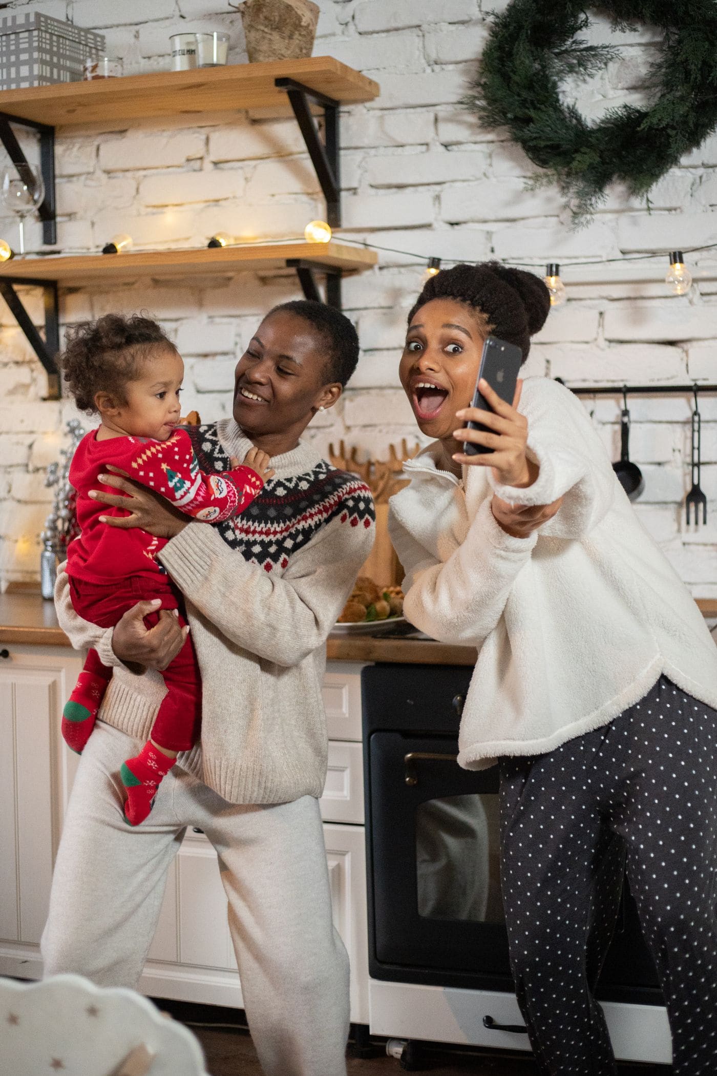 Two women and a baby smiling at a phone during a video call in a kitchen